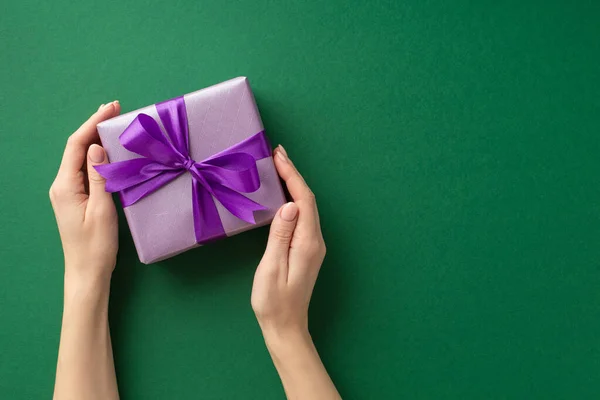 圣诞节的概念 第一人称头像女性手拿着紫罗兰彩带蝴蝶结紫丁香礼盒的照片 背景为孤立的绿色 有彩色背景 — 图库照片
