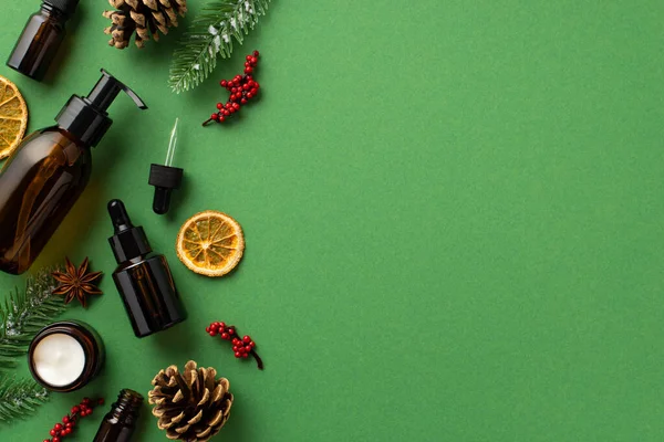 stock image Natural cosmetics concept. Top view photo of pump dropper bottles cream jar fir branches in frost pine cones mistletoe berries anise and dried orange slices isolated green background with blank space