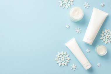 Kış sezonu kozmetik konsepti. Etiket krem kavanozları ve kar tanesi süslemeleri olmayan beyaz tüplerin, izole açık mavi arka planda fotosu.