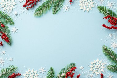 Yeni yıl konsepti. Karla kaplı ökseotu böğürtlenli çam ağacı dallarının ve izole edilmiş pastel mavi arka planda kar tanesi süslemelerinin en üst görüntüsü. Ortasında boşluk var.