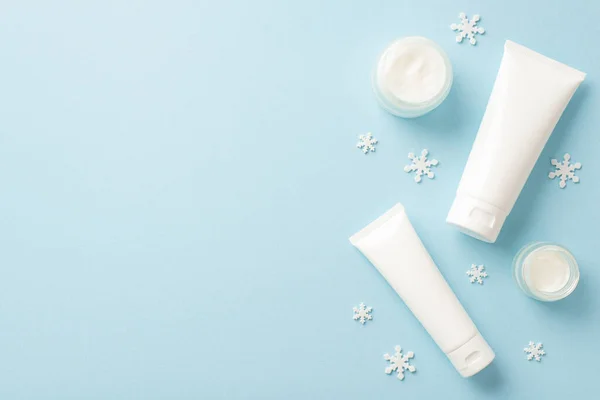 Winter season skin care concept. Top view photo of white tubes without label cream jars and snowflakes on isolated pastel blue background with copyspace