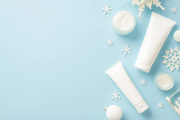 Winter skin care cosmetics concept. Top view photo of tubes without label cream jars white baubles and snowflake ornaments on isolated pastel blue background with copyspace
