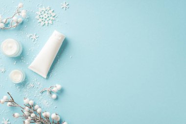 Kışın cilt bakımı kozmetik konsepti. Etiketsiz krem beyaz losyon kavanozlarının en üst görüntüsü. Kar taneleri izole edilmiş açık mavi arka planda kar tohumları eker ve bitki dalları yerleştirir.