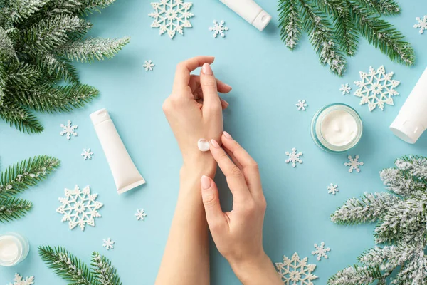 stock image Winter season skin care concept. First person top view photo of woman using hand cream cosmetic jars tubes snowflakes and spruce branches in hoarfrost on isolated pastel blue background with copyspace