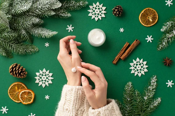 stock image Winter skin care concept. First person top view photo of girl in sweater using hand cream jar fir branches in frost pine cones dried citrus slices cinnamon snowflakes on isolated green background