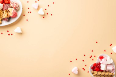 Sevgililer Günü kutlaması konsepti. Kalp şeklindeki fincan tabakları, şekerli kurabiyeler, jöle şekerler ve izole edilmiş bej arka planda boş alan konfetileri.