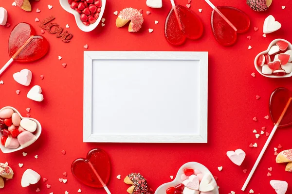 stock image Valentine's Day concept. Top view photo of white photo frame and heart shaped saucers with sweets candies lollipops on isolated red background with copyspace