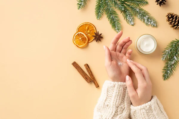 stock image First person top view photo of woman in jumper using hand cream small jar spruce branches dried orange slices pine cone cinnamon sticks and anise on isolated pastel beige background with empty space