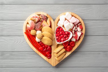 Sevgililer Günü konsepti. Tahta kalp şeklindeki servis tepsisinin en üst görüntüsü. Çikolata jöleli kurabiyeler ve gri tahta masa arkasında cam bardak içilen içecekler.