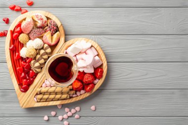 Sevgililer Günü konsepti. Tahta kalp şeklindeki servis tepsisinin en üst görüntüsü. Çikolatalı jöleli kurabiyeler ve gri ahşap masa zemininde bir bardak içecek.