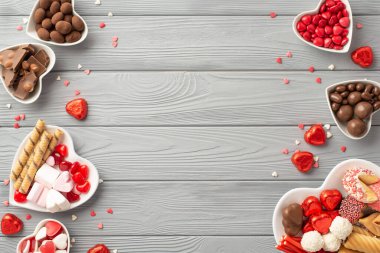 Sevgililer Günü konsepti. Kalp şeklindeki çanak çömlek, çikolatalı jöleli kurabiyeler ve gri tahta masa zemininde konfeti.