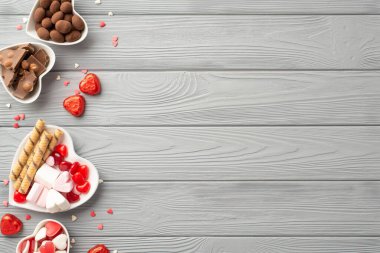 Sevgililer Günü konsepti. Kalp şeklindeki sofra takımının, çikolatalı jöleli kurabiyelerin ve konfetilerin gri ahşap masa arkaplanının fotosu.