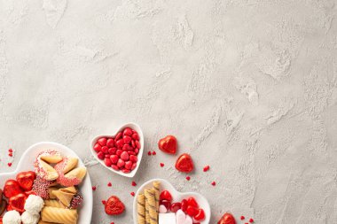 Sevgililer Günü konsepti. Kalp şeklindeki tabakların, çikolatalı jöleli kurabiyelerin ve beton desenli arka planda boş alan konfetisinin en üst görüntüsü.