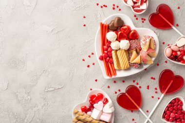 Sevgililer Günü kutlaması konsepti. Kalp şeklindeki lolipopların jöle şekerli lolipop tabakları ve telif uzaylı beton doku arka planında konfetilerin üst görünümü