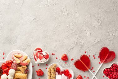 Sevgililer Günü konsepti. En üstteki fotoğrafta kalp şeklinde tabaklar, çikolatalı jöle şekerlemeler, lolipoplar ve beton desenli konfeti, boş alan.