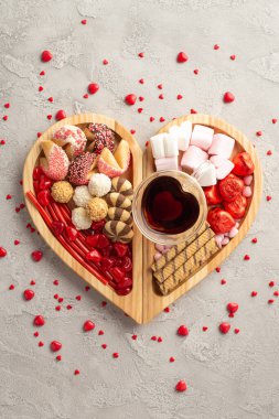 Sevgililer Günü konsepti. Tahta kalbin dikey fotoğrafı servis tepsisi şekerlemeli kurabiye bardağı ve beton dokuda konfeti.