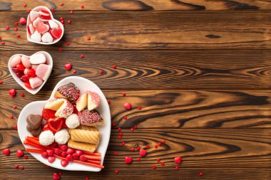 Sevgililer Günü konsepti. Tahta masa arkaplanında içi boş şekerlemeli ve kurabiyeli kalp şeklindeki çay tabakları ve kurabiyelerin üst görünümü