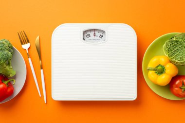Kilo verme konsepti. Karabiber çanağı, lahana karnabahar ve çatal bıçak takımlarının izole edilmiş turuncu arka planda en üstteki fotoğrafı.
