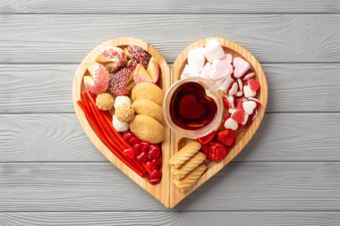 Sevgililer Günü konsepti. Tahta kalp şeklindeki servis tepsisinin en üst görüntüsü. Çikolata jöleli kurabiyeler ve gri tahta masa arkasında cam bardak içilen içecekler.