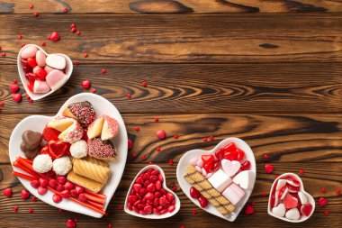 Sevgililer Günü kutlaması konsepti. Kalp şeklindeki tabakların, şekerleme ve çerezlerin ahşap masa arkasında fotokopi alanı olan en iyi görüntüsü.