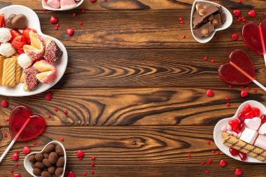 Sevgililer Günü konsepti. Kalp şeklindeki tabakların en üst görüntüsü. Çikolata jöleli şekerler, lolipoplar ve ahşap masa arkasında boş alan olan kurabiyeler.