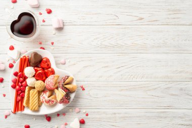 Sevgililer Günü kutlaması konsepti. Kalp şeklindeki cam bardağın en üst görüntüsü. İçme kabı, çikolatalı jöle şekerlemeleri ve beyaz ahşap masa zemininde, kopyalanmış pasta.