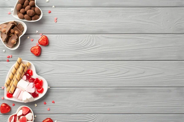 Sevgililer Günü konsepti. Kalp şeklindeki sofra takımının, çikolatalı jöleli kurabiyelerin ve konfetilerin gri ahşap masa arkaplanının fotosu.