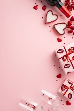 Sevgililer Günü konsepti. Şarap şişesi kadehlerinin dikey fotoğrafı mevcut konfeti kutuları ve izole edilmiş pastel pembe arka planda kalp şeklinde mumlar.