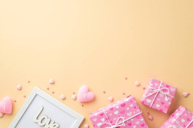 Sevgililer Günü konsepti. Üst görünüm fotoğraf pembe hediye kutuları ambalaj kağıdında, içinde kalp desenli fotoğraf çerçevesi yazıtları aşk mumları ve izole edilmiş bej arkaplan üzerine serpiştirmeler