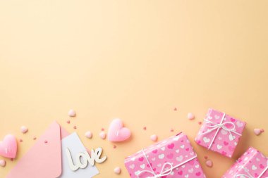 Sevgililer Günü konsepti. Kalbin desenli zarf ile ambalaj kağıdına sarılı pembe hediye kutularının en üstteki fotoğrafında izole edilmiş bej arkaplanda aşk mumları ve serpintiler var.