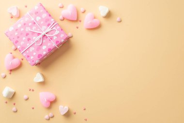 Sevgililer Günü konsepti. Pembe hediye kutusu kalbinin en üstteki fotoğrafı izole edilmiş pastel bej arka planda şekerleme mumları ve serpiştirilmiş şekerlemeler.