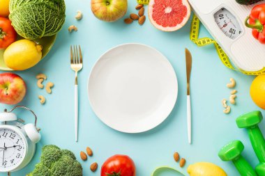 Sağlıklı beslenme konsepti. Tabak çatal bıçak takımının üst görüntüsü sebze, fındık çalar saat halterleri ve kopyalanmış pastel mavi arka planda bant ölçüsü.