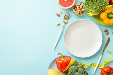 Uygun diyet konsepti. Sebzeli çatal bıçak tabaklarının üst görüntüsü lahana biberi, kaju fıstığı ve izole edilmiş pastel mavi arka planda mezura.