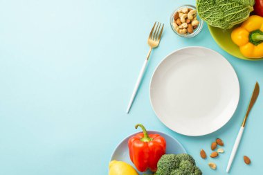 Uygun diyet konsepti. Sebzeli çatal bıçak tabaklarının üst görüntüsü lahana biber bademleri ve izole edilmiş pastel mavi arka planda kaju.