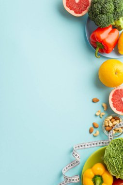 Zayıflatıcı konsept. Üst görünümde meyve ve sebzeli tabaklar, lahana, lahana, karabiber, kaju ve izole edilmiş pastel mavi arka planda mezura ve mezura.
