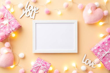 Sevgililer Günü konsepti. Fotoğraf çerçevesi hediye kutularının, kabarık kalp şekilli oyuncakların en üstteki fotoğrafı. Yazıtlar seni seviyor. Ampul çelengi ve yumuşak ponponlar, izole edilmiş pastel bej arka plan, boş alan.