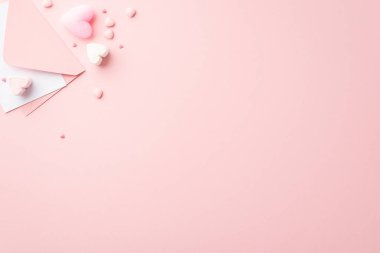 Sevgililer Günü konsepti. Zarfın en üstteki fotoğrafında kalp şeklinde şekerlemeler ve izole edilmiş pastel pembe arka planda kopyalanmış şekerler var.