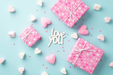 Sevgililer Günü konsepti. Pembe hediye kutularının en üstteki fotoğrafı kalp şeklinde lokum mumları yazılar seni seviyor ve izole edilmiş açık mavi arkaplana serpiştiriyor.