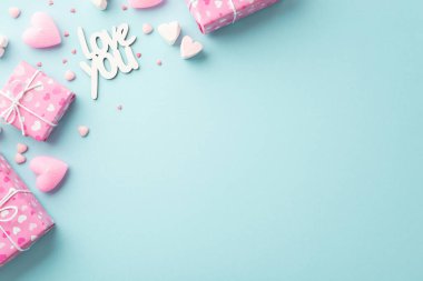 Sevgililer Günü konsepti. Paket kağıdındaki pembe hediye kutularının en üstteki fotoğrafında kalp desenli lokum yazıtları seni seviyor ve izole edilmiş açık mavi arkaplan üzerine boş alan serpiştiriyor.