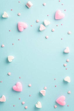 Sevgililer Günü konsepti. Kalp şeklindeki şekerlemelerin dikey fotoğrafı ve izole edilmiş pastel mavi arkaplan üzerine serpiştirilmiş şekerlemeler ortada kopyalanmış boşluk