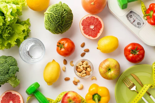 Proper nutrition concept. Top view photo of vegetables fruits nuts glass of water plate cutlery dumbbells tape measure and scales on isolated white background