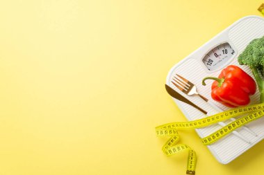 Kilo verme konsepti. Çan biberi karnabahar çatal bıçak takımının ve ölçüm bantlarının izole edilmiş pastel sarısı arka planda ve kopyalanmış