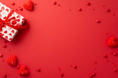 Sevgililer Günü konsepti. Hediye kutusu kalp şeklindeki en üst görüntü fotoğrafı mumlar ve serpintiler izole edilmiş kırmızı arkaplanda ortada boş bir alan ile
