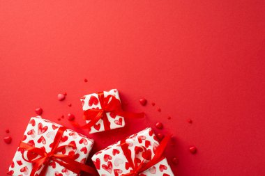 Sevgililer Günü konsepti. Hediye kutularının ve kalp şeklindeki parçaların izole edilmiş kırmızı arkaplandaki telif boşluğuyla en üstteki görüntüsü