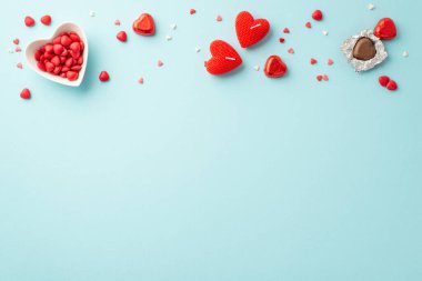 Sevgililer Günü konsepti. Kalp şeklindeki fincan tabağının en üstteki fotoğrafı çikolata parçacıkları serpiştirilmiş ve mumlar izole edilmiş açık mavi arka planda, kopyalanmış