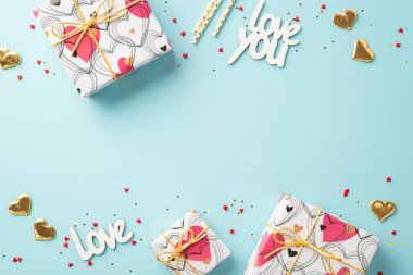 Sevgililer Günü konsepti. Şimdiki kutuların en üstteki fotoğrafı altın kalpler yazıtlar sizi seviyor izole edilmiş pastel mavi arkaplandaki boş alanlara saman ve süslemeler serpiştiriyor