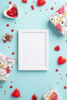 Sevgililer Günü konsepti. Fotoğraf çerçevesi hediye kutularının dikey üst görüntüsü kalp şeklinde fincan tabağı şekerlemeleri ve izole edilmiş pastel arkaplan üzerindeki mumlar boş alan