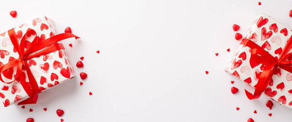 Valentine's Day concept. Top view photo of two gift boxes in wrapping paper with heart pattern and sprinkles on isolated white background with blank space