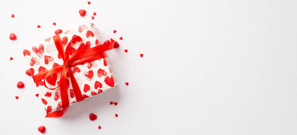 St Valentine's Day concept. Top view photo of giftbox in wrapping paper with heart pattern and sprinkles on isolated white background with empty space