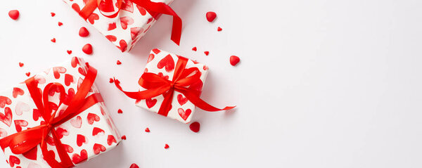 Valentine's Day concept. Top view photo of gift boxes with red ribbon bows and heart shaped sprinkles on isolated white background with blank space